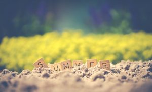A picture containing the word summer in scrabble letters on some sand.