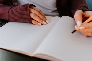 Photo of person writing on a notepad with a pen. Photo by Kelly Sikkema on Unsplash